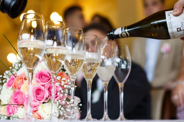 Man pours champagne in the glasses standing before a wedding bouquet on the table